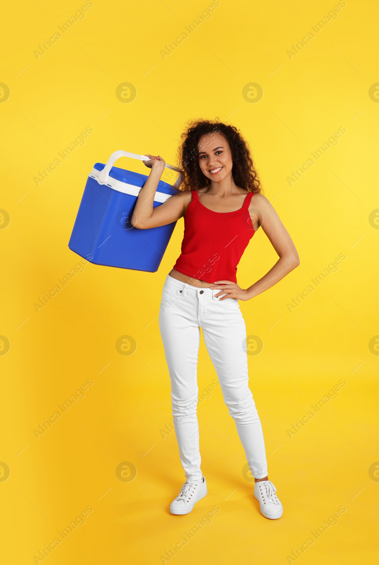 Photo of Happy young African American woman with cool box on yellow background