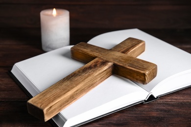 Cross, Bible and burning candle on wooden background, closeup. Christian religion