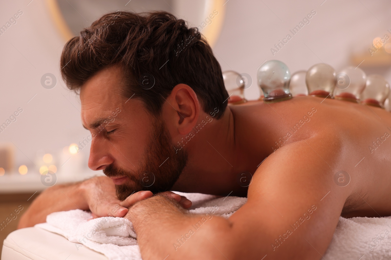 Photo of Cupping therapy. Man with glass cups on massage couch in spa salon