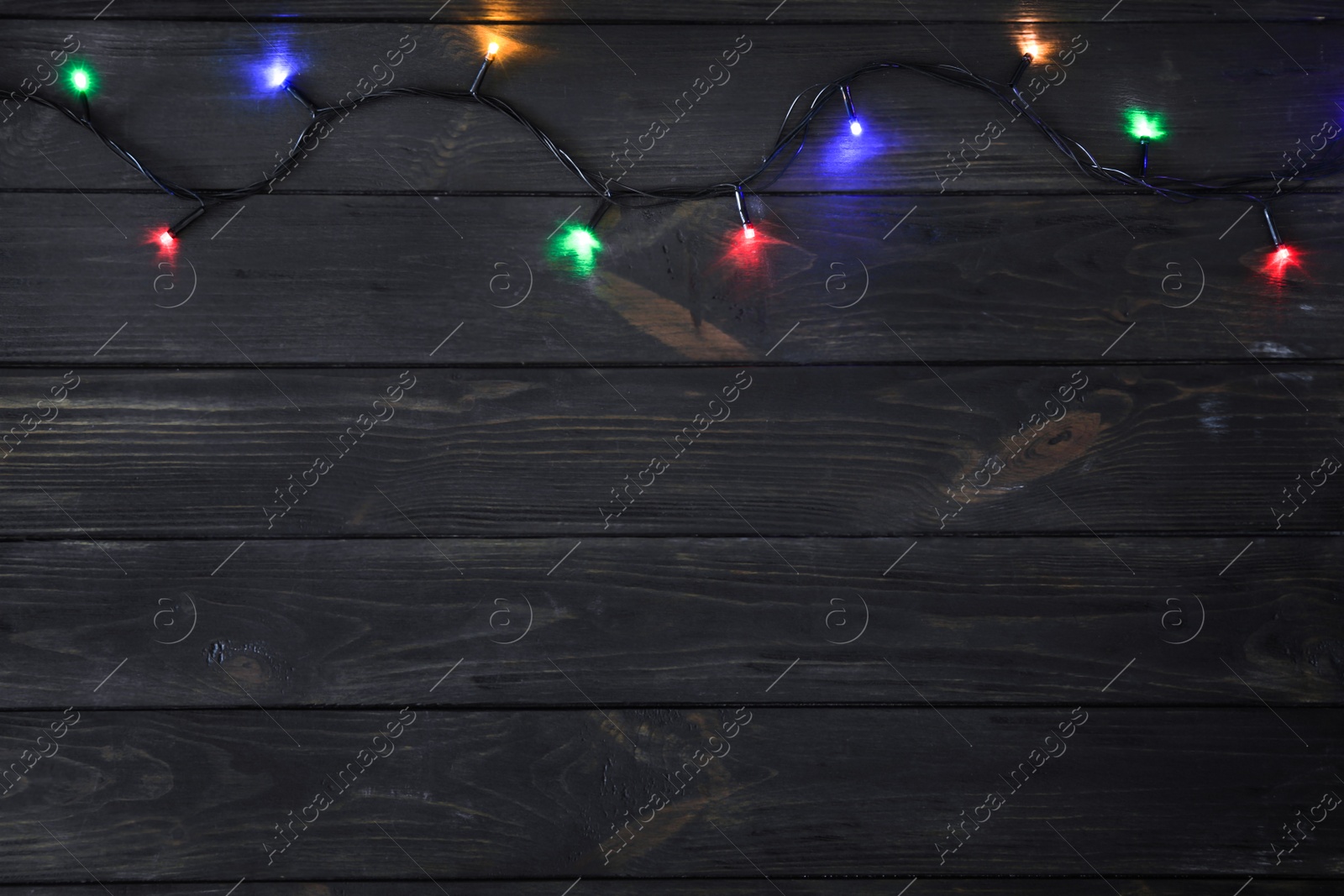 Photo of Glowing Christmas lights on dark wooden background, top view. Space for text