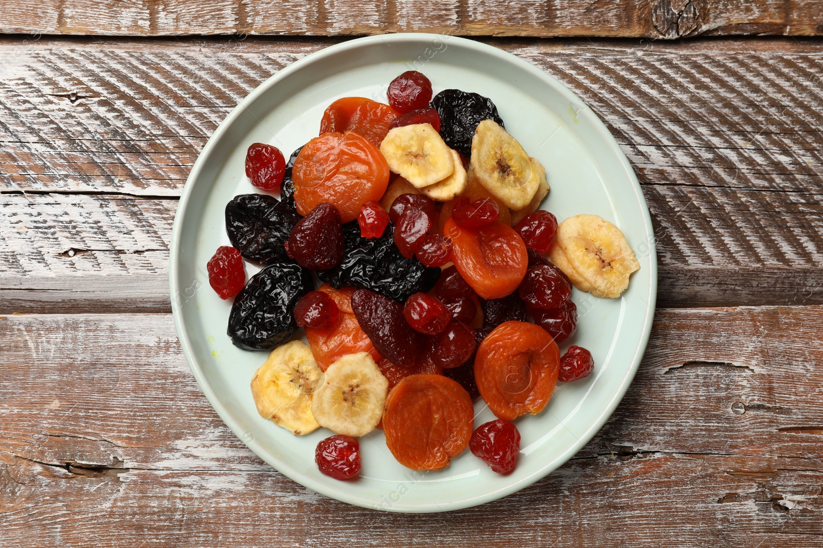 Photo of Mix of delicious dried fruits on wooden table, top view