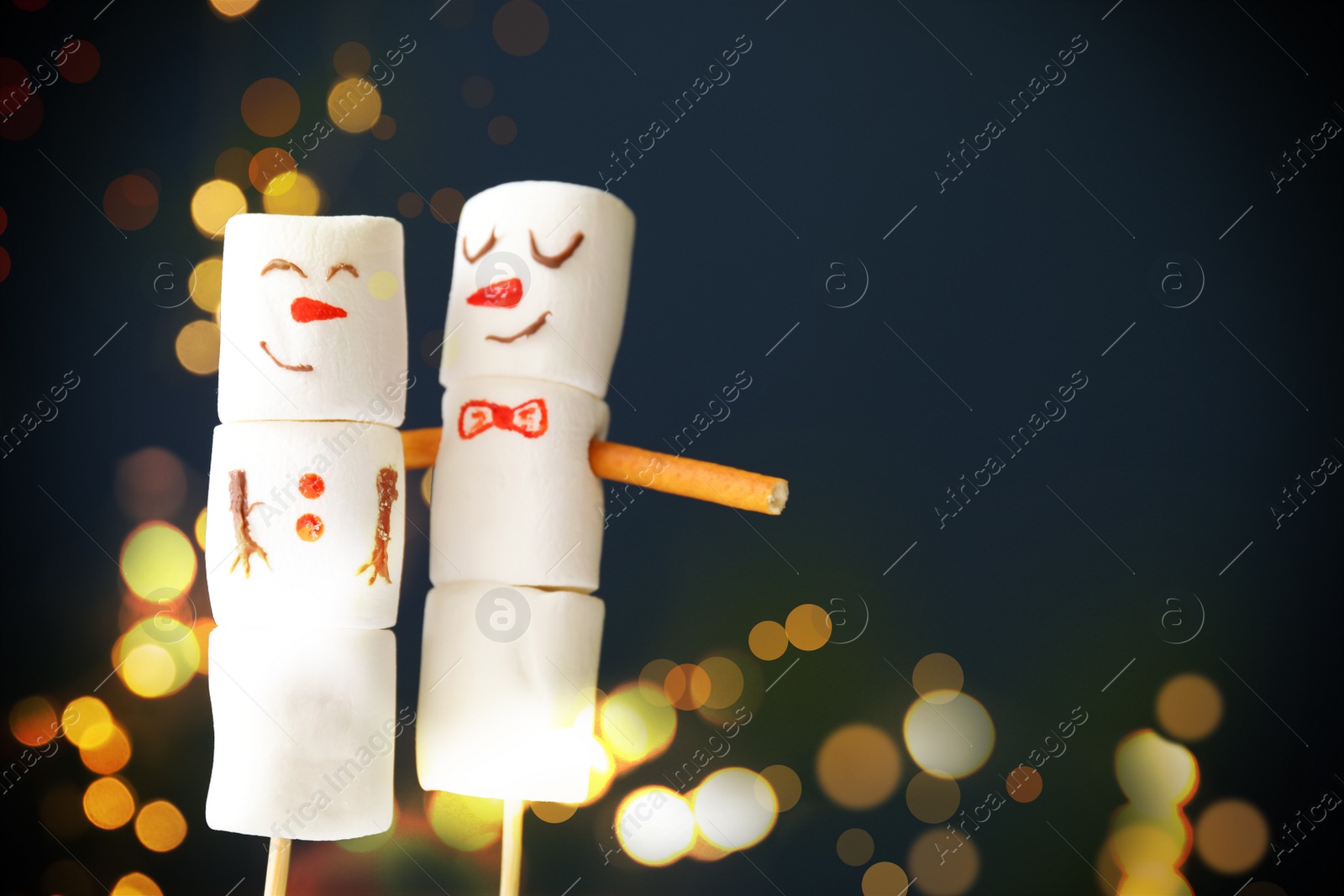 Image of Funny snowmen made of marshmallows on dark blue background, space for text. Bokeh effect