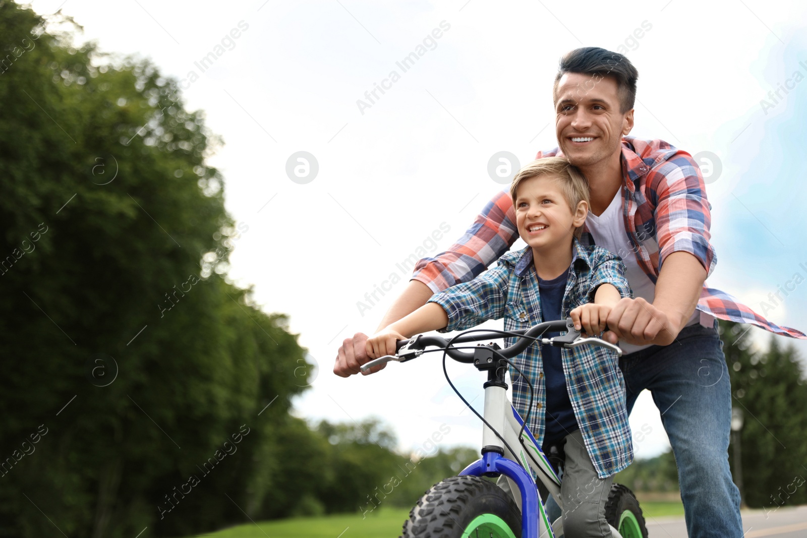 Image of Dad teaching son to ride bicycle outdoors