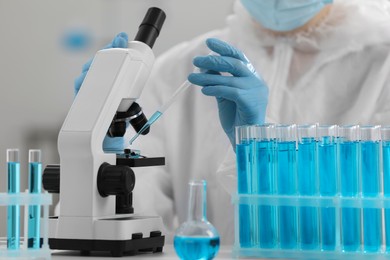 Scientist dripping sample onto Petri dish while working with microscope in laboratory, closeup