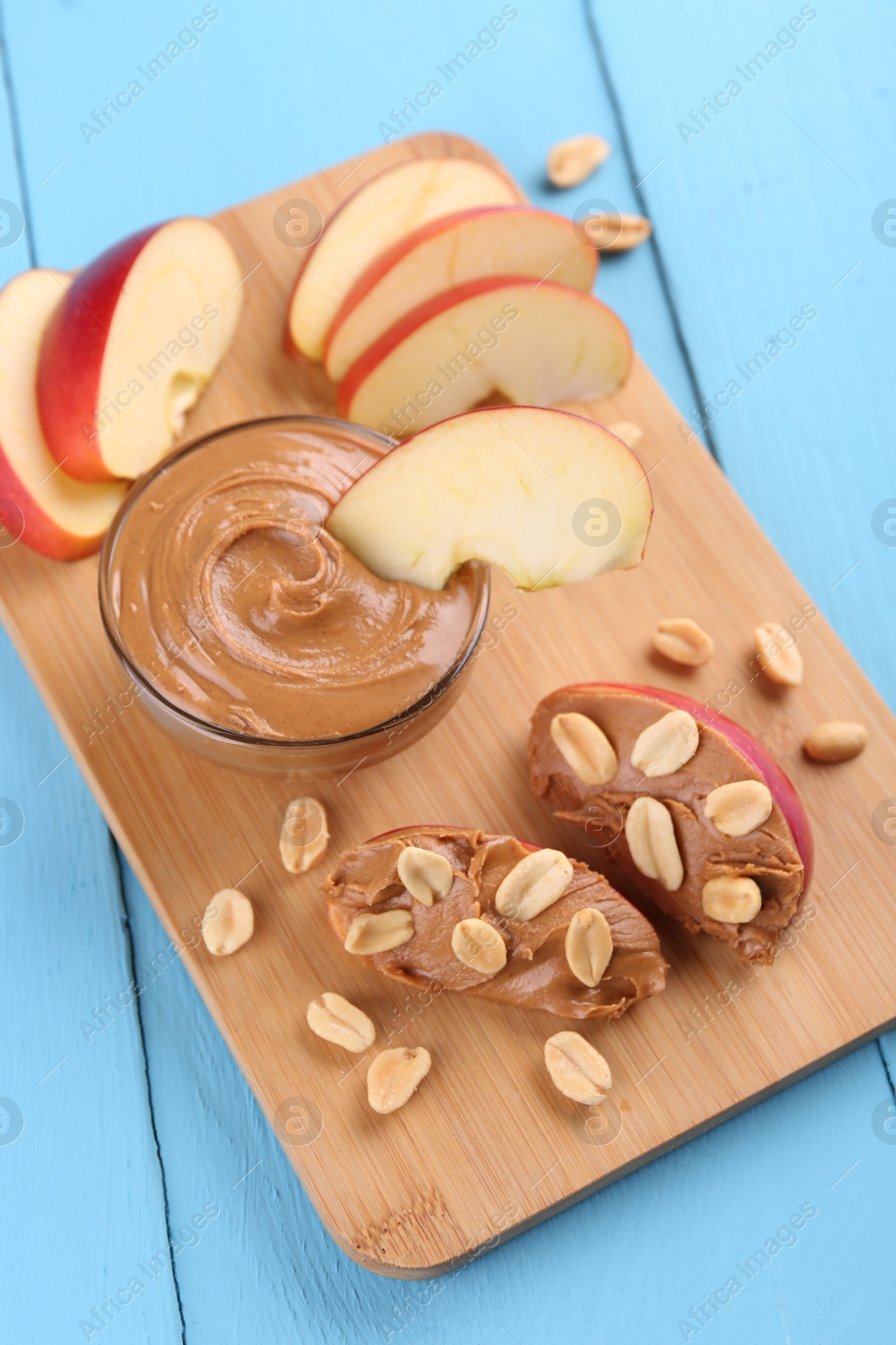 Photo of Slices of fresh apple with peanut butter and nuts on light blue wooden table, above view