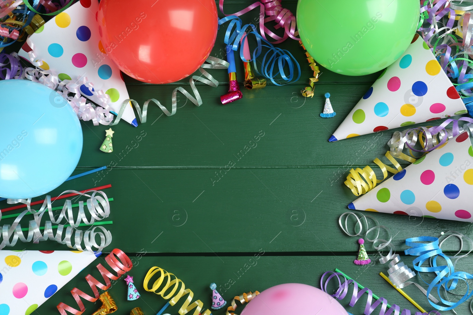 Photo of Frame of colorful serpentine streamers and other party accessories on green wooden background, flat lay. Space for text