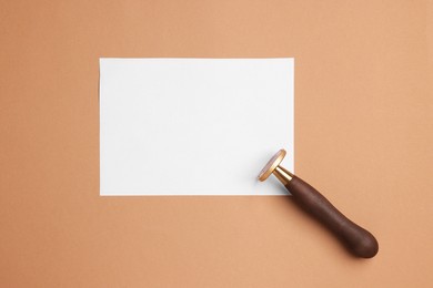 Photo of One stamp tool and sheet of paper on light brown background, top view. Space for text