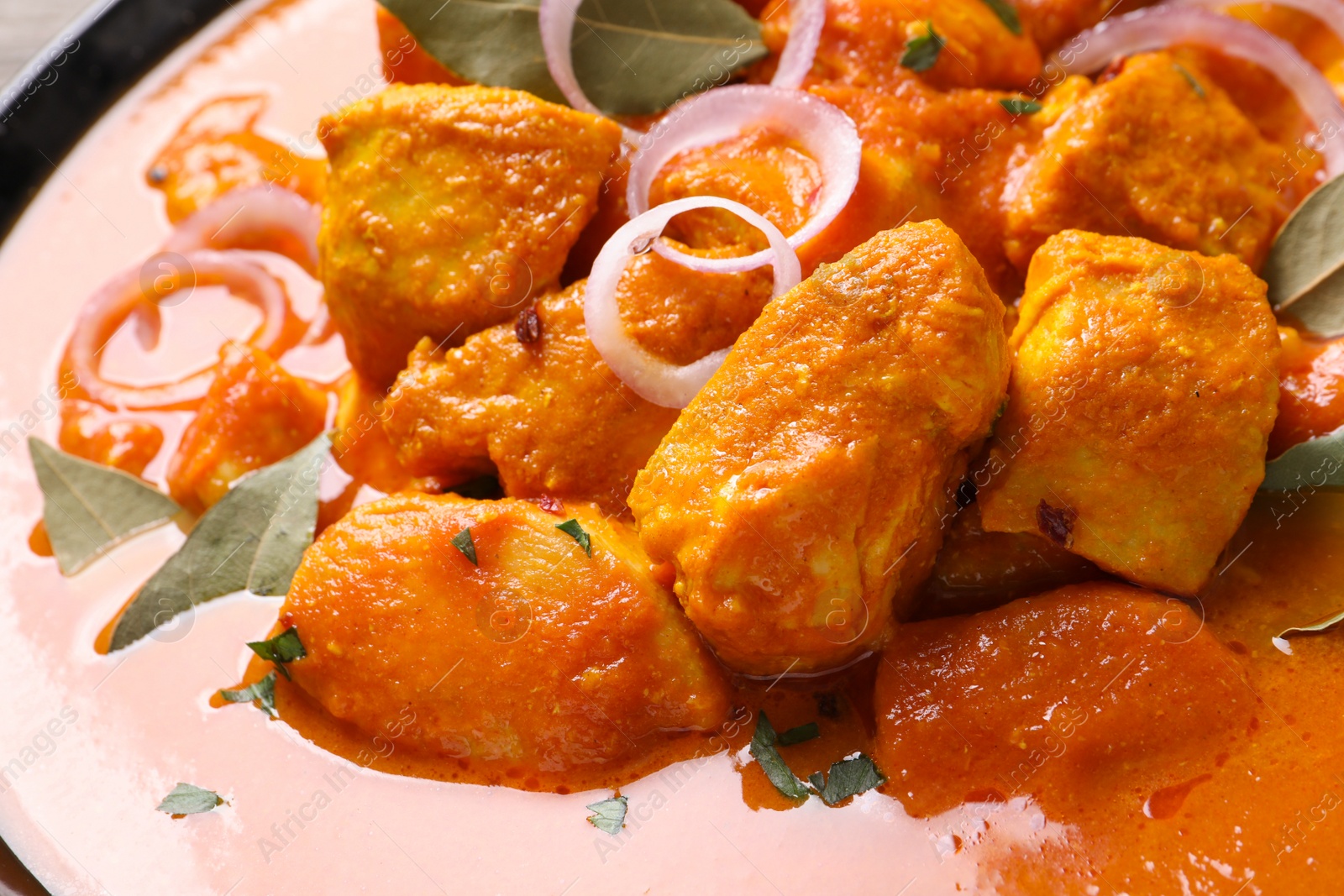 Photo of Delicious chicken curry with onion rings and bay leaves, closeup