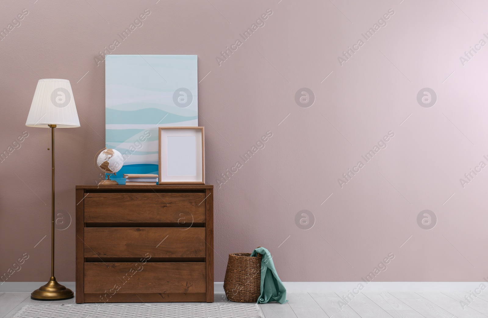 Photo of Wooden chest of drawers with globe, books and empty frame near beige wall in room, space for text. Interior design