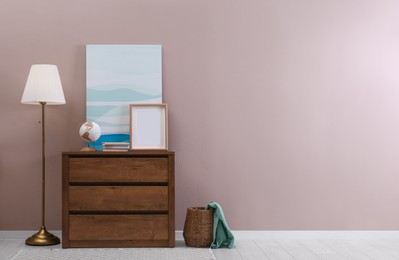 Photo of Wooden chest of drawers with globe, books and empty frame near beige wall in room, space for text. Interior design
