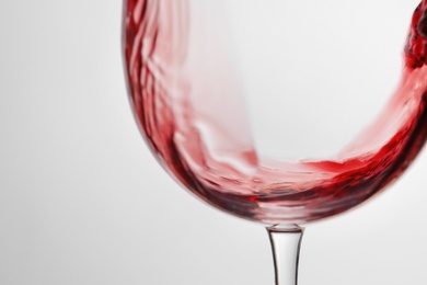 Pouring red wine into glass on light background, closeup