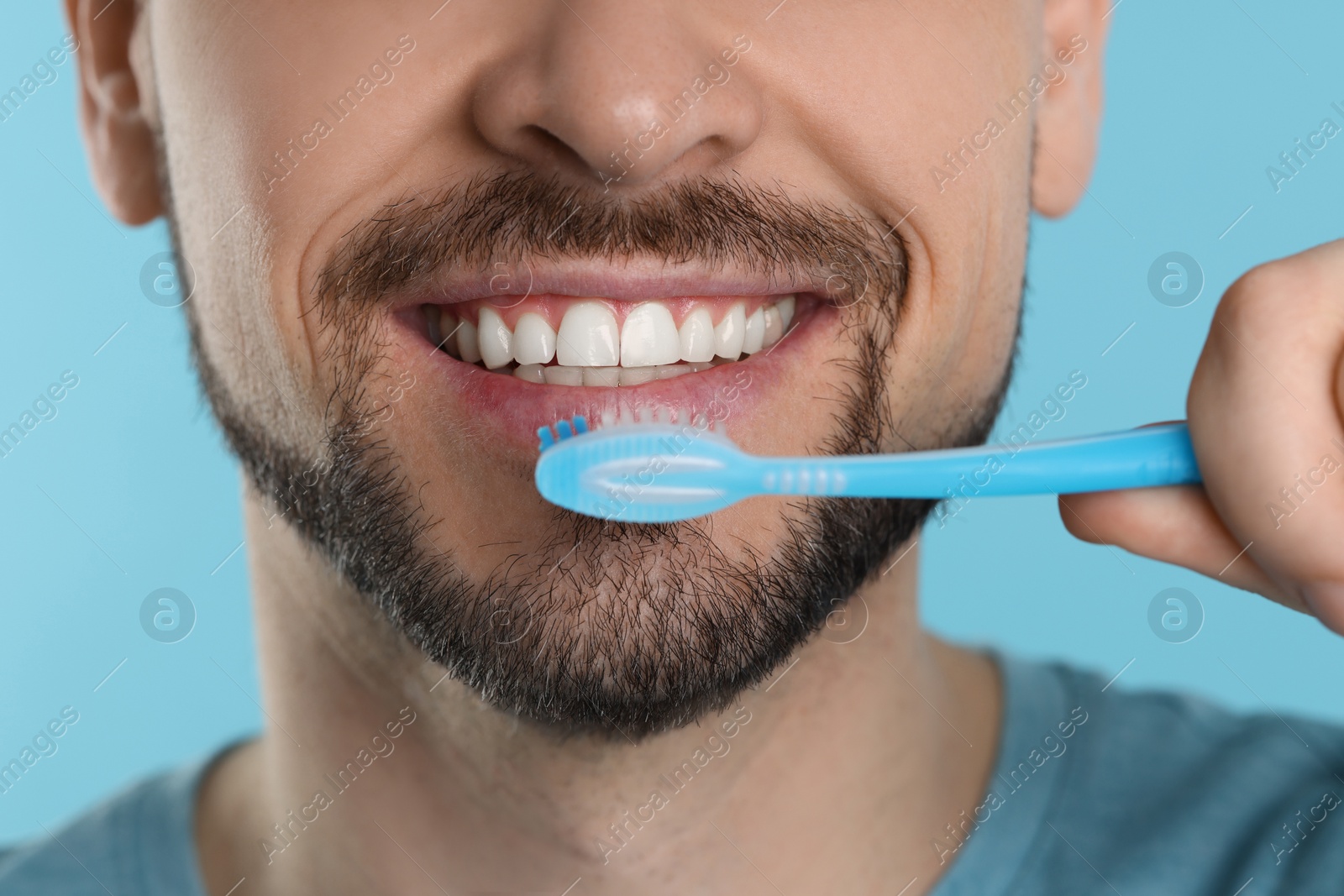 Photo of Man brushing his teeth with plastic toothbrush on light blue background, closeup