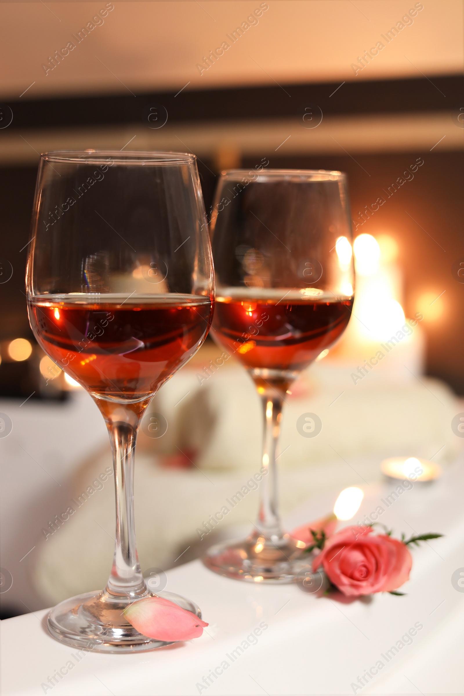 Photo of Wine in glasses and rose on edge of bath indoors, closeup. Romantic atmosphere