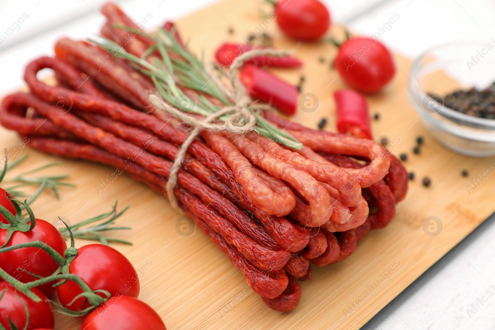 Photo of Bundle of delicious kabanosy with tomatoes and rosemary on white wooden table, closeup