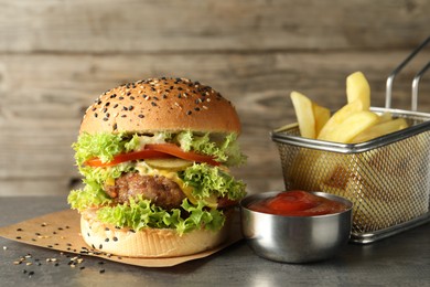 Photo of Burger with delicious patty, french fries and sauce on gray table