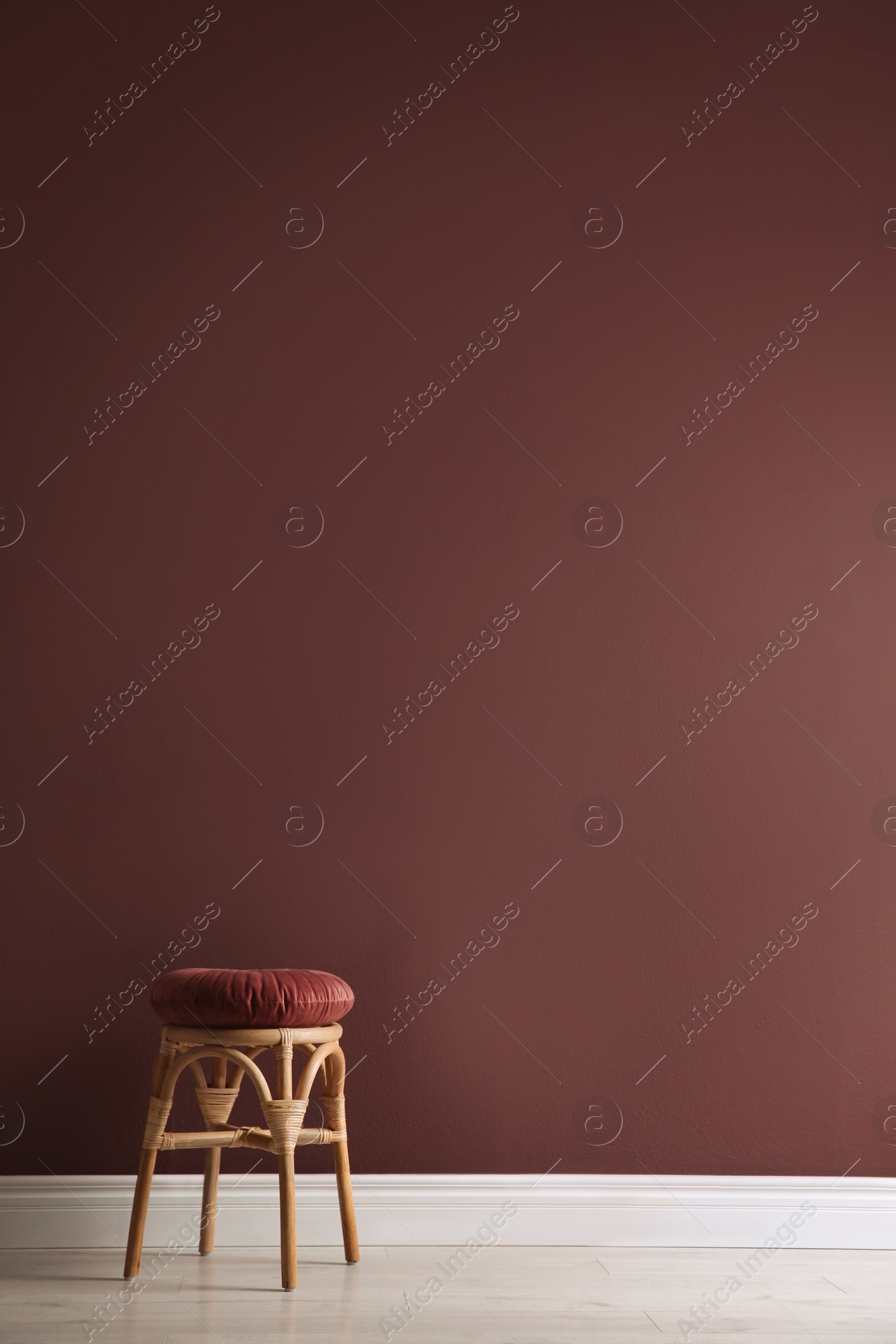 Photo of Stylish wooden stool with cushion near color wall, space for text. Interior element