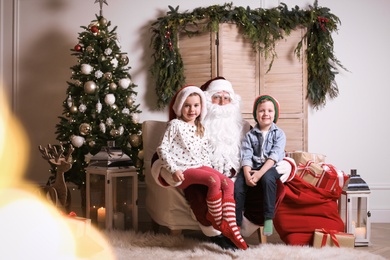 Photo of Santa Claus with little children in photo zone decorated for Christmas