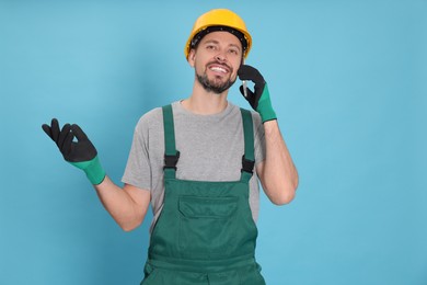 Photo of Professional repairman in uniform talking on phone against light blue background