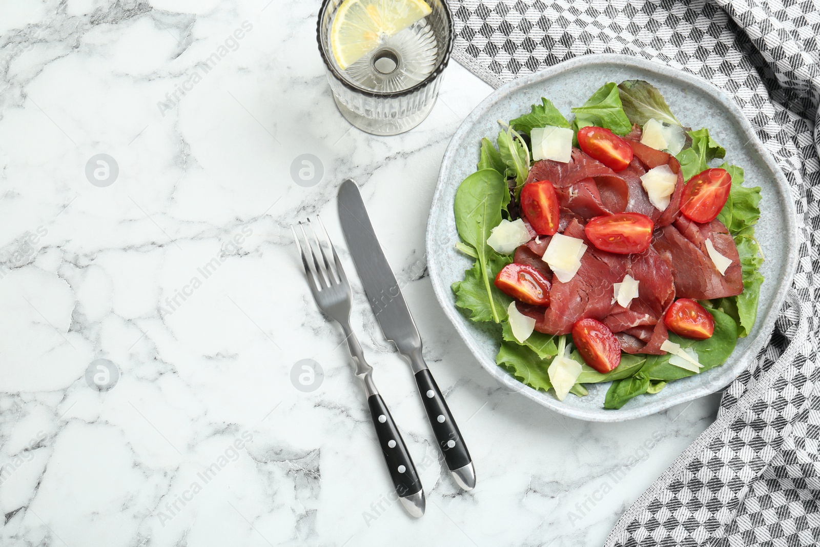 Photo of Delicious bresaola salad with tomatoes and parmesan cheese served on white marble table, flat lay. Space for text