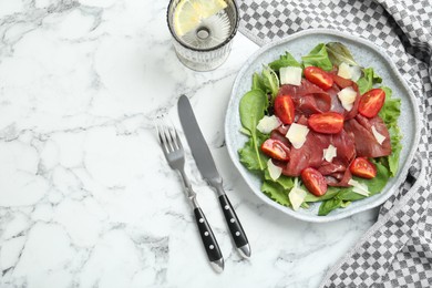 Delicious bresaola salad with tomatoes and parmesan cheese served on white marble table, flat lay. Space for text