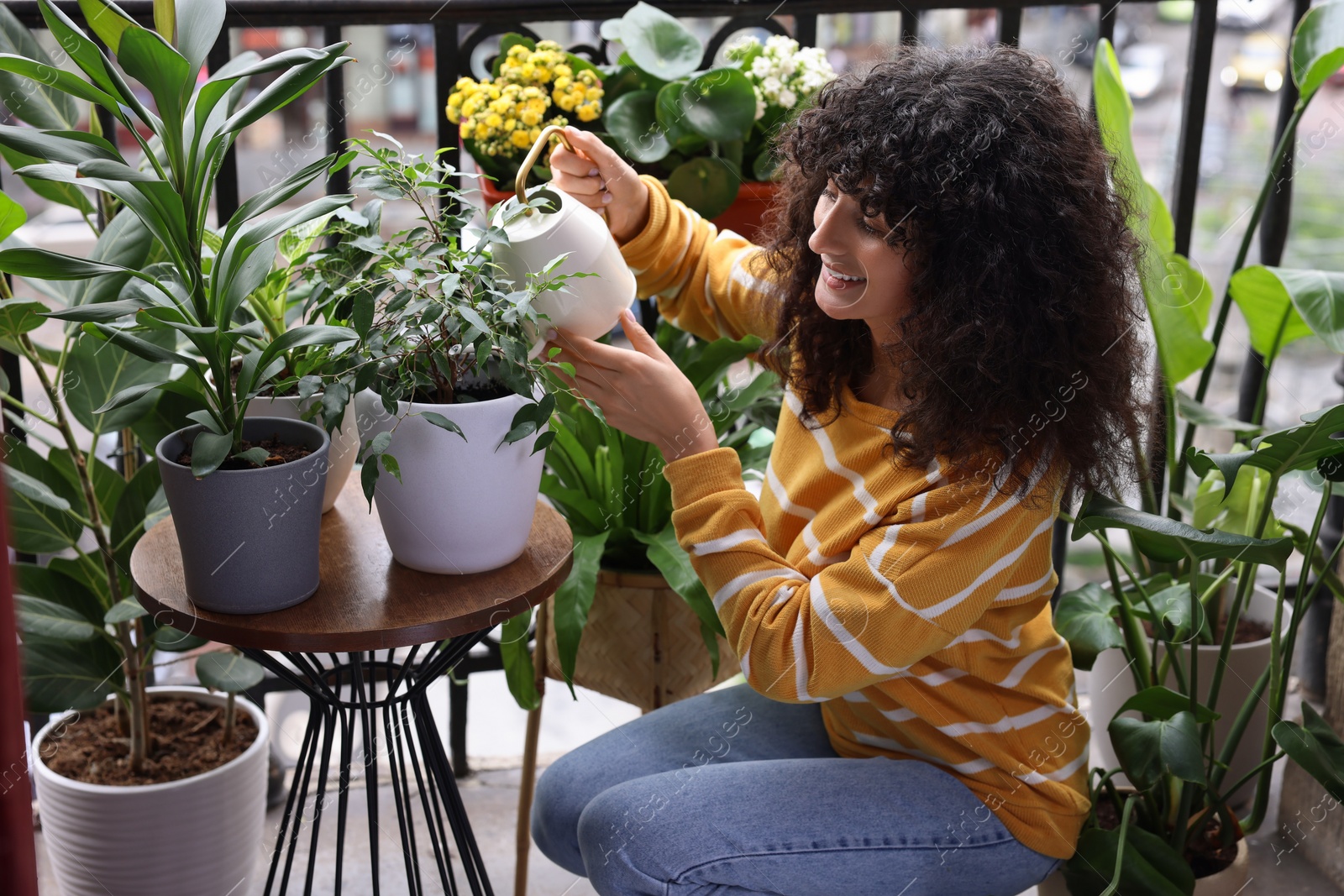 Photo of Beautiful young woman watering green houseplants on balcony