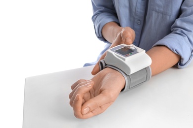 Woman checking blood pressure with sphygmomanometer at table against white background, closeup. Cardiology concept