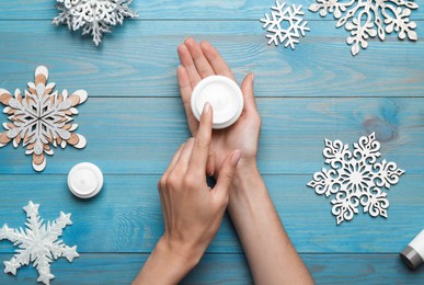 Woman with jar of hand cream at turquoise wooden table, top view