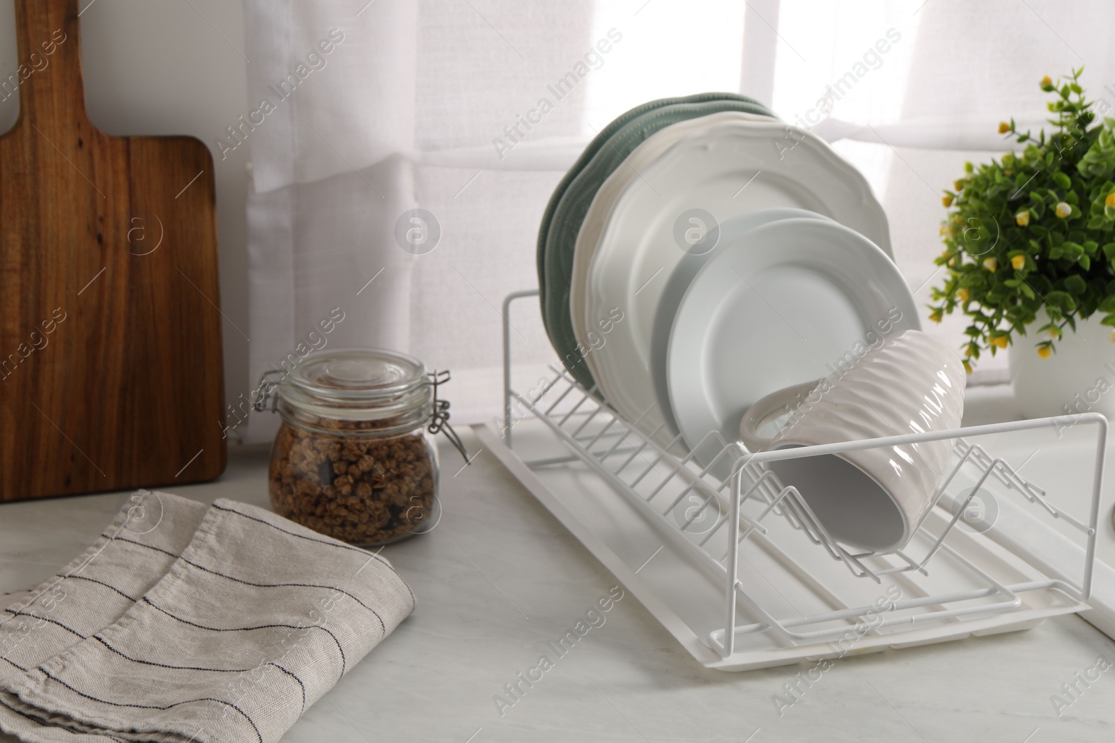 Photo of Drainer with different clean dishware and cup on light table indoors