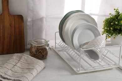 Drainer with different clean dishware and cup on light table indoors