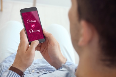 Image of Man visiting dating site via smartphone indoors, closeup