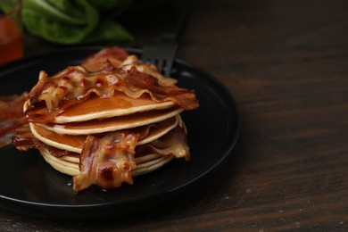 Photo of Delicious pancakes with fried bacon served on wooden table, closeup. Space for text