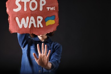 Photo of Woman holding poster with words Stop the War on black background. Space for text