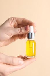 Photo of Woman holding bottle of cosmetic oil on beige background, closeup