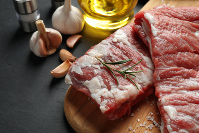 Photo of Raw ribs with rosemary and salt on black table, closeup