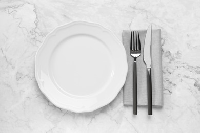 Photo of Clean plate and shiny silver cutlery on white marble table, flat lay