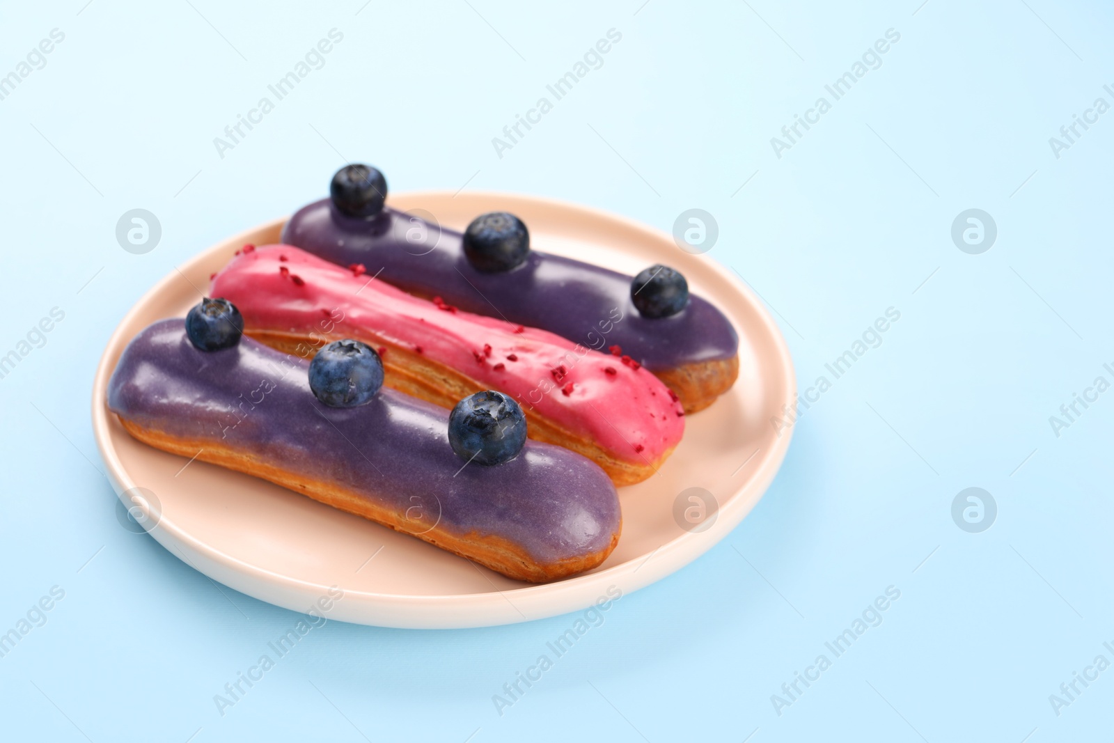 Photo of Delicious eclairs covered with glaze on light blue background. Space for text