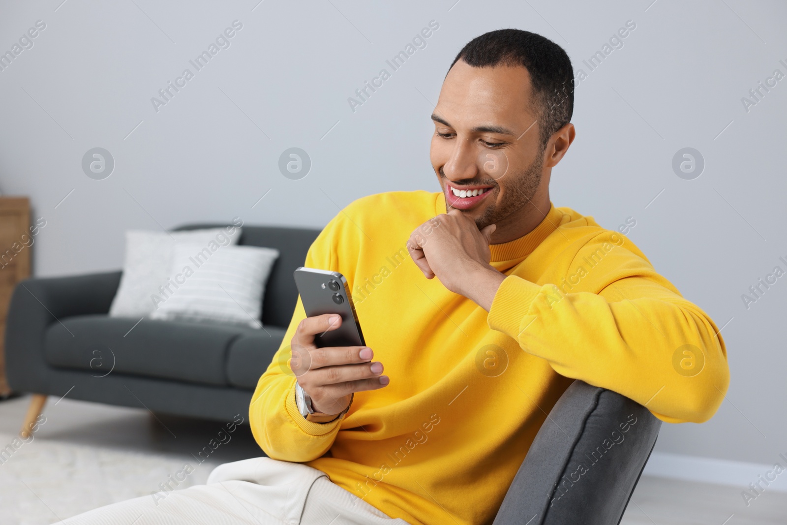 Photo of Happy man sending message via smartphone indoors