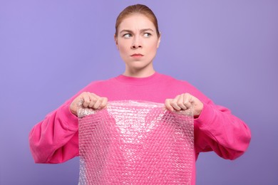 Angry woman popping bubble wrap on purple background. Stress relief