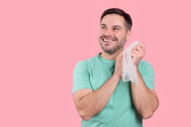 Happy man with bubble wrap on pink background. Space for text