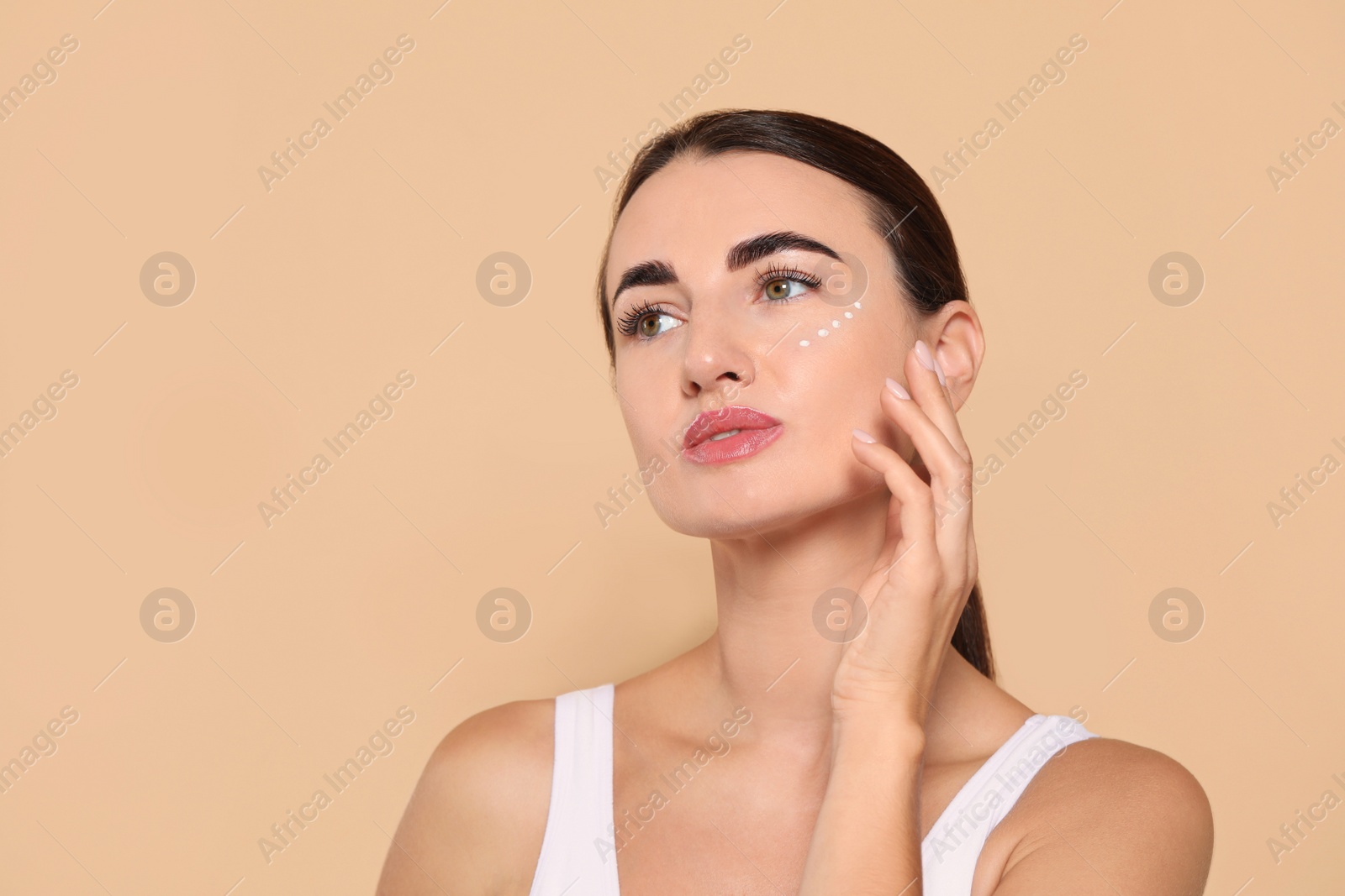 Photo of Woman with cosmetic product around eye on beige background. Space for text