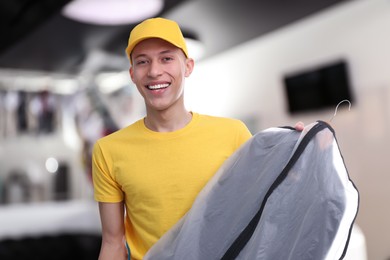Happy courier holding garment cover with clothes in dry-cleaning