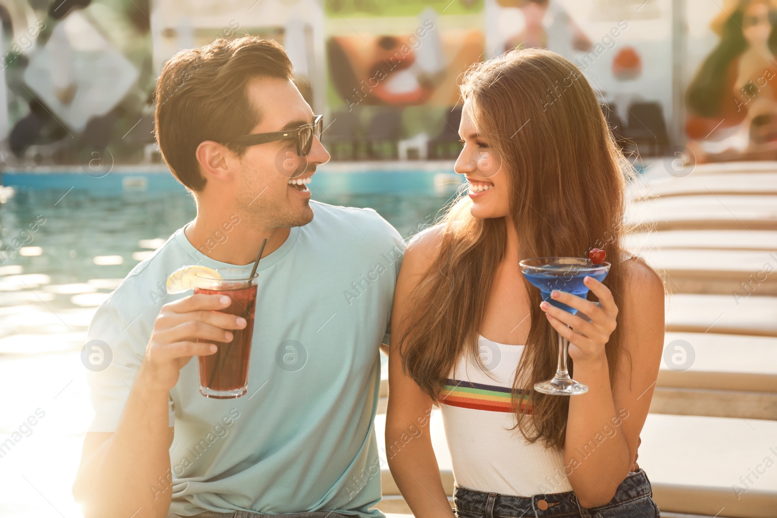 Photo of Happy young couple with fresh summer cocktails relaxing near swimming pool