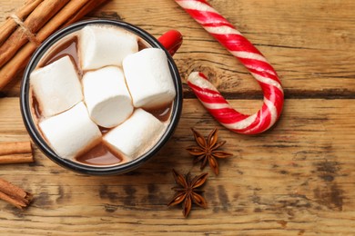 Photo of Tasty hot chocolate with marshmallows, candy cane and spices on wooden table, flat lay