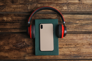 Book, modern headphones and smartphone on wooden table, flat lay