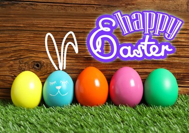 Image of Happy Easter. One egg with drawn face and ears as bunny among others on green grass against wooden background