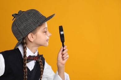 Photo of Cute little detective with magnifying glass on yellow background. Space for text