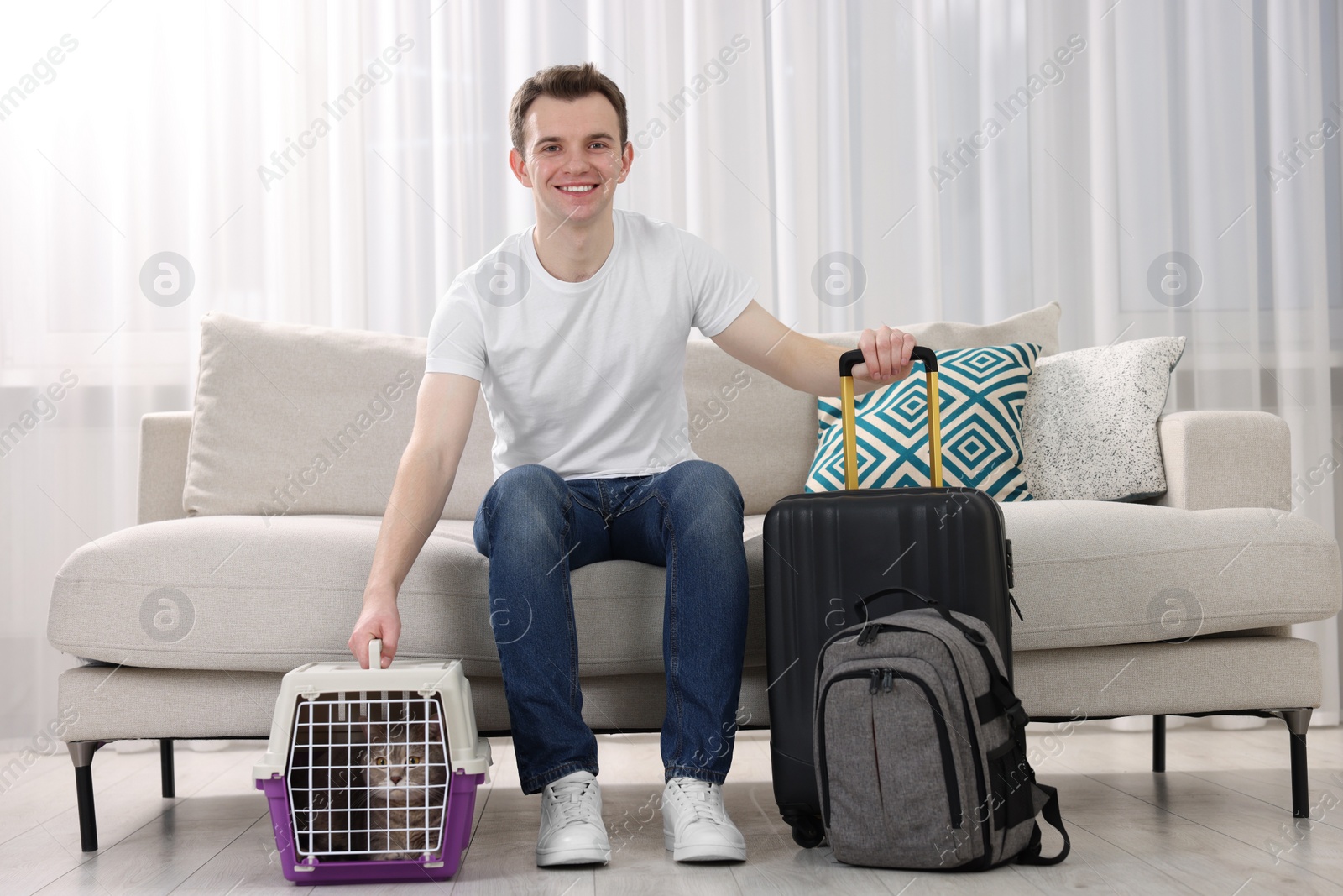 Photo of Travel with pet. Man near carrier with cute cat on sofa at home