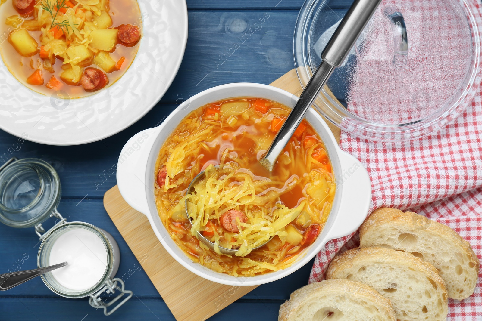 Photo of Delicious sauerkraut soup with smoked sausages served on blue wooden table, flat lay