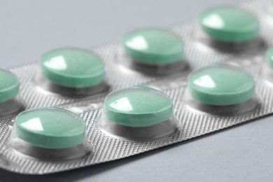 Photo of Green pills in blister on grey background, closeup