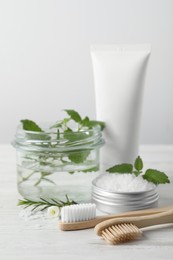 Toothbrushes, dental products and herbs on white wooden table